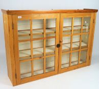A pine kitchen wall unit with two shelves behind glazed double doors,