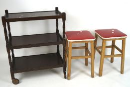 Two retro stools upholstered in red plastic, and a dark stained tea trolley with three shelves,