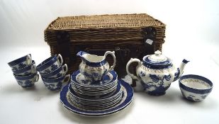 A vintage wicker picnic basket containing a selection of Booth's old willow pattern ceramics,