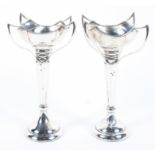 A pair of Edwardian arts and crafts silver vases, each with four flowing handles,