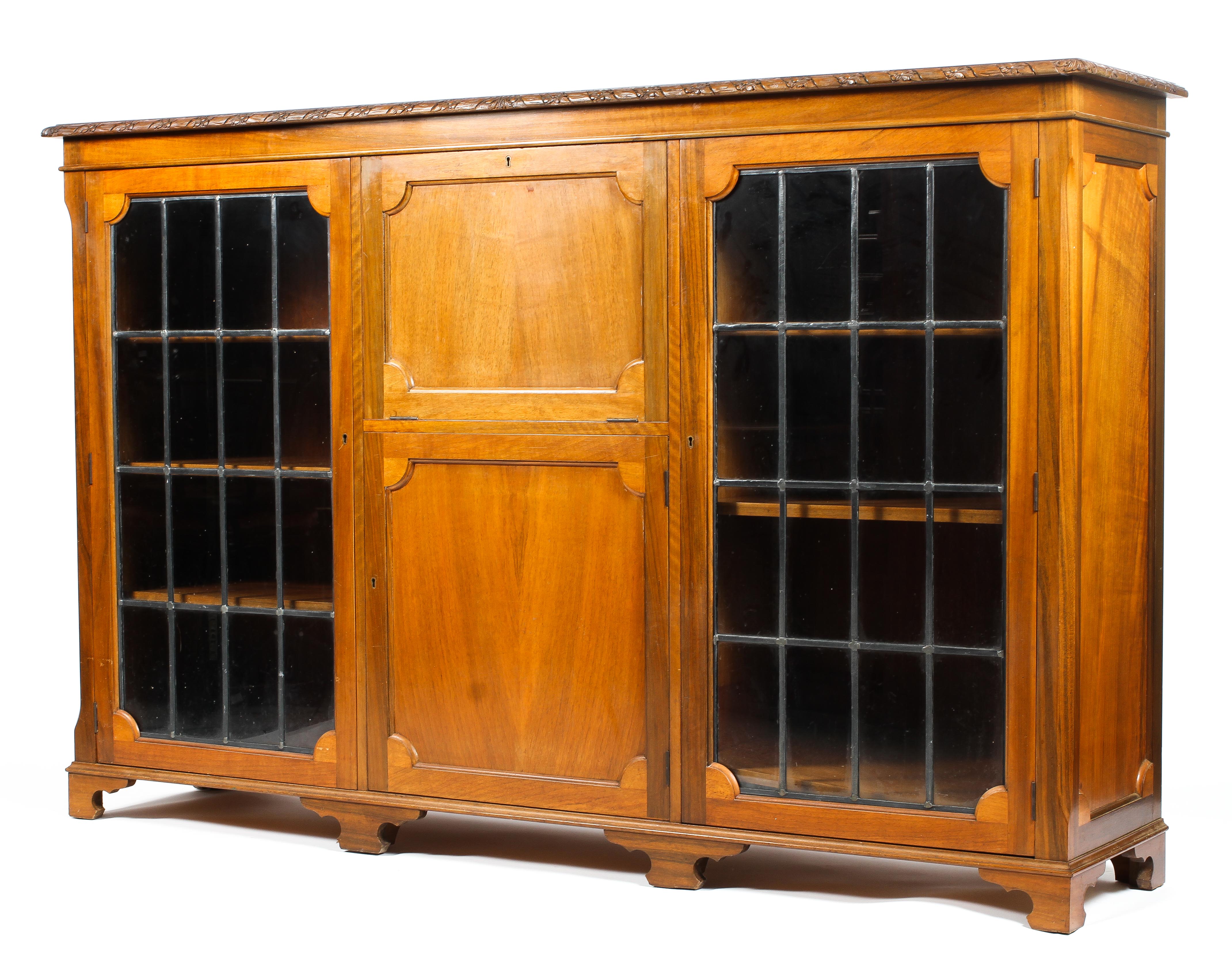 An Edwardian walnut sideboard with carved frieze above a central fall front and cupboard flanked by