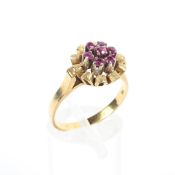 An 18ct gold and ruby set daisy ring, seven free cut rubies in a textured petal surround mount, 5g,