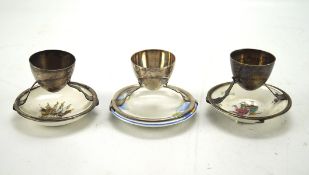 Three Christopher Dresser eggcups, each attached to a ceramic plate of assorted designs, height 6.