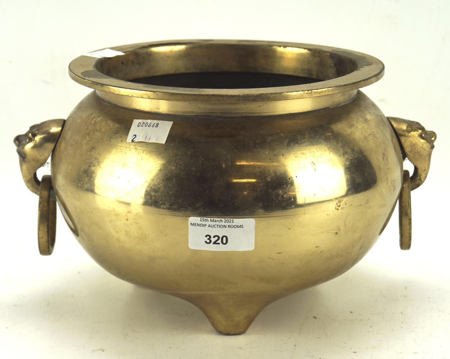 A 20th century brass censor, raised upon three small feet, with two face shaped ring pull handles,