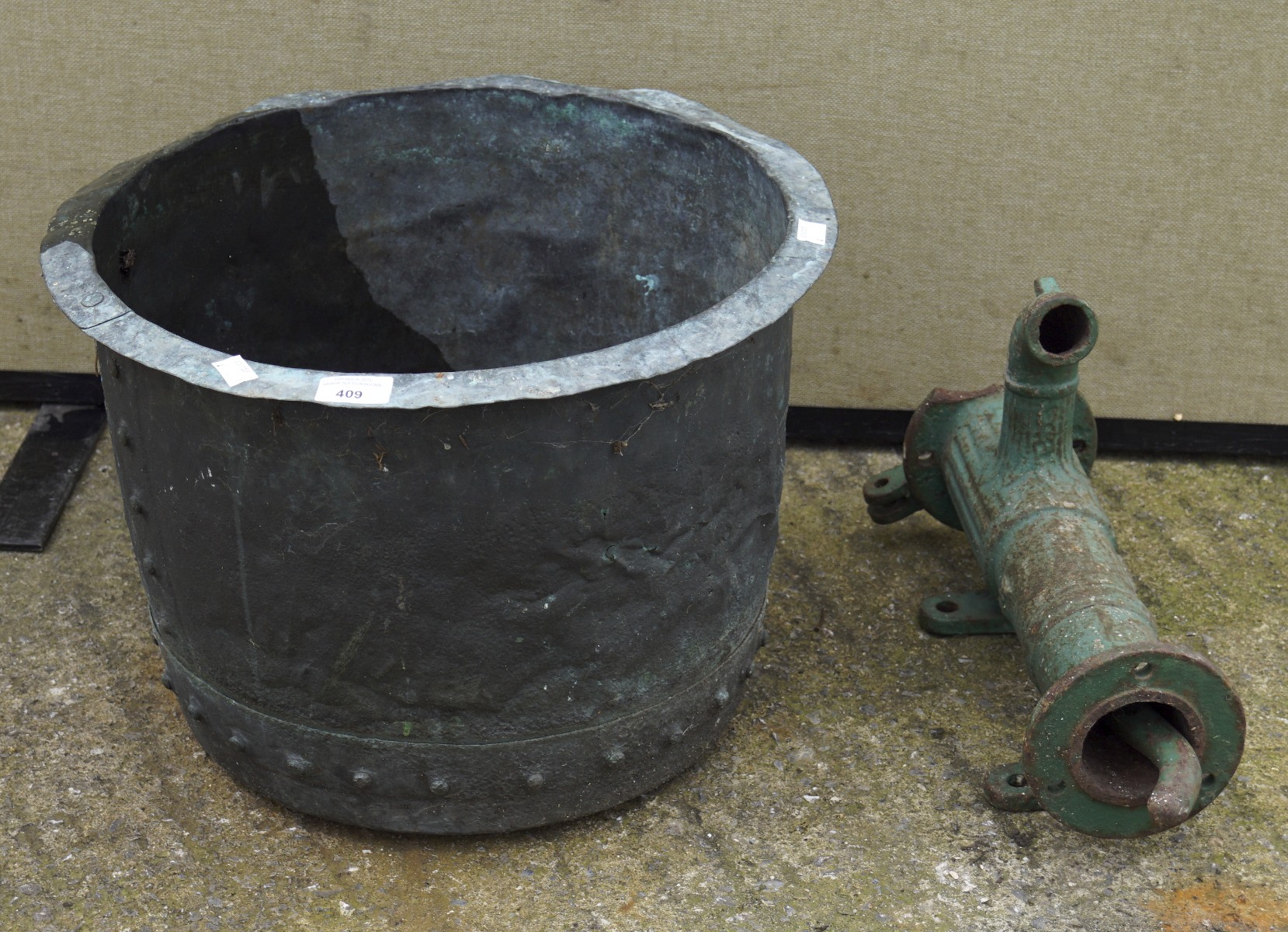 An antique metal pot and a water pump, both cast metal,