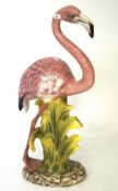 A large glazed ceramic figure depicting a Pink Flamingo, stood amongst foliage,