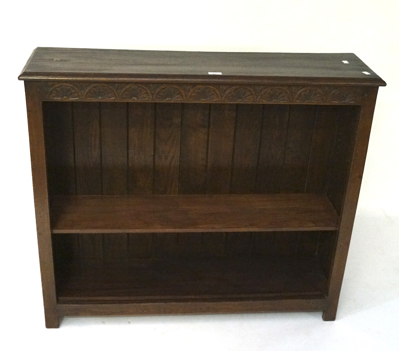 An oak bookcase with carved half flower border to the top, with two shelves