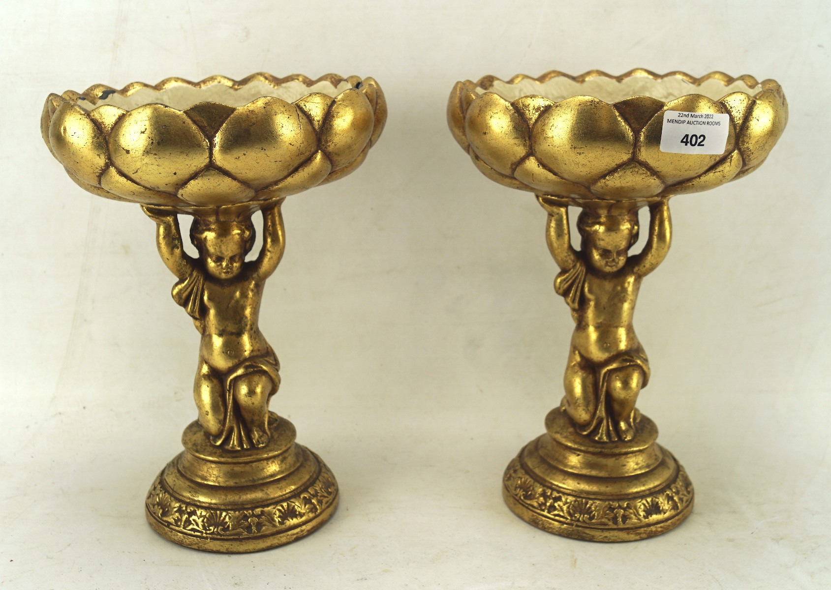 A contemporary pair of gilt comports in the form of kneeling boys holding a lotus flower,