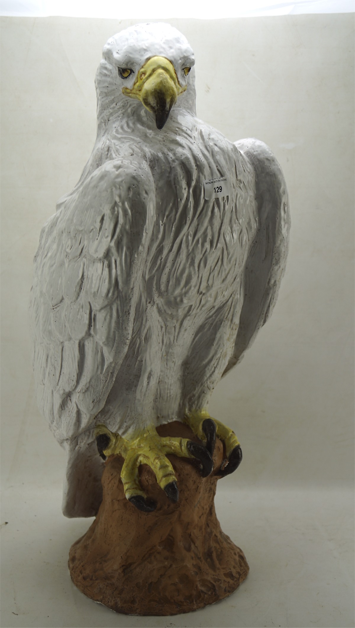 A large ceramic model of a white feathered bird of prey perching on a rock,