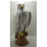 A large ceramic model of a white feathered bird of prey perching on a rock,