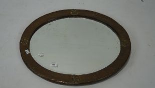 An arts and crafts copper mounted wall mirror, of oval form, adorned with floral motifs,