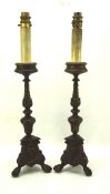 A pair of bronzed candlesticks on a tripod claw and ball foot, fitted for electricity,