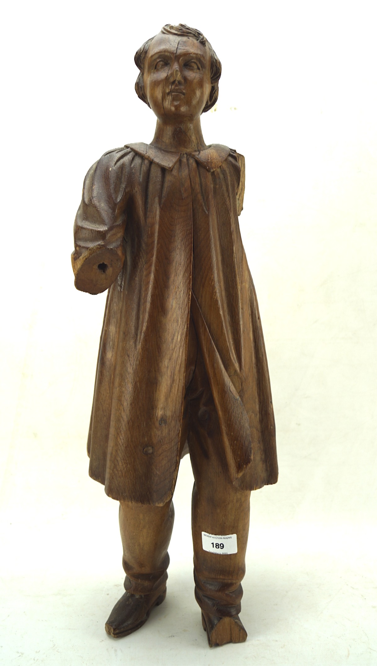 Large carved wooden figure of a young boy in a long collared coat,