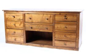 A 19thC pine shop counter, of two central drawers and open shelf, flanked by eight drawers 4+4,