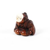 A 19th century wood netsuke of a man in a patterned robe crouching and wearing an ivory usofuki