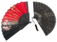 Two 20th century folding fans, one with with a black and red fabric leaf painted with flowers,