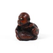 A 19th century wood netsuke of a blind man crouching and clasping a large stone, one eye inlaid,