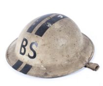 A military helmet, painted in white and marked "BS" and striped in black,