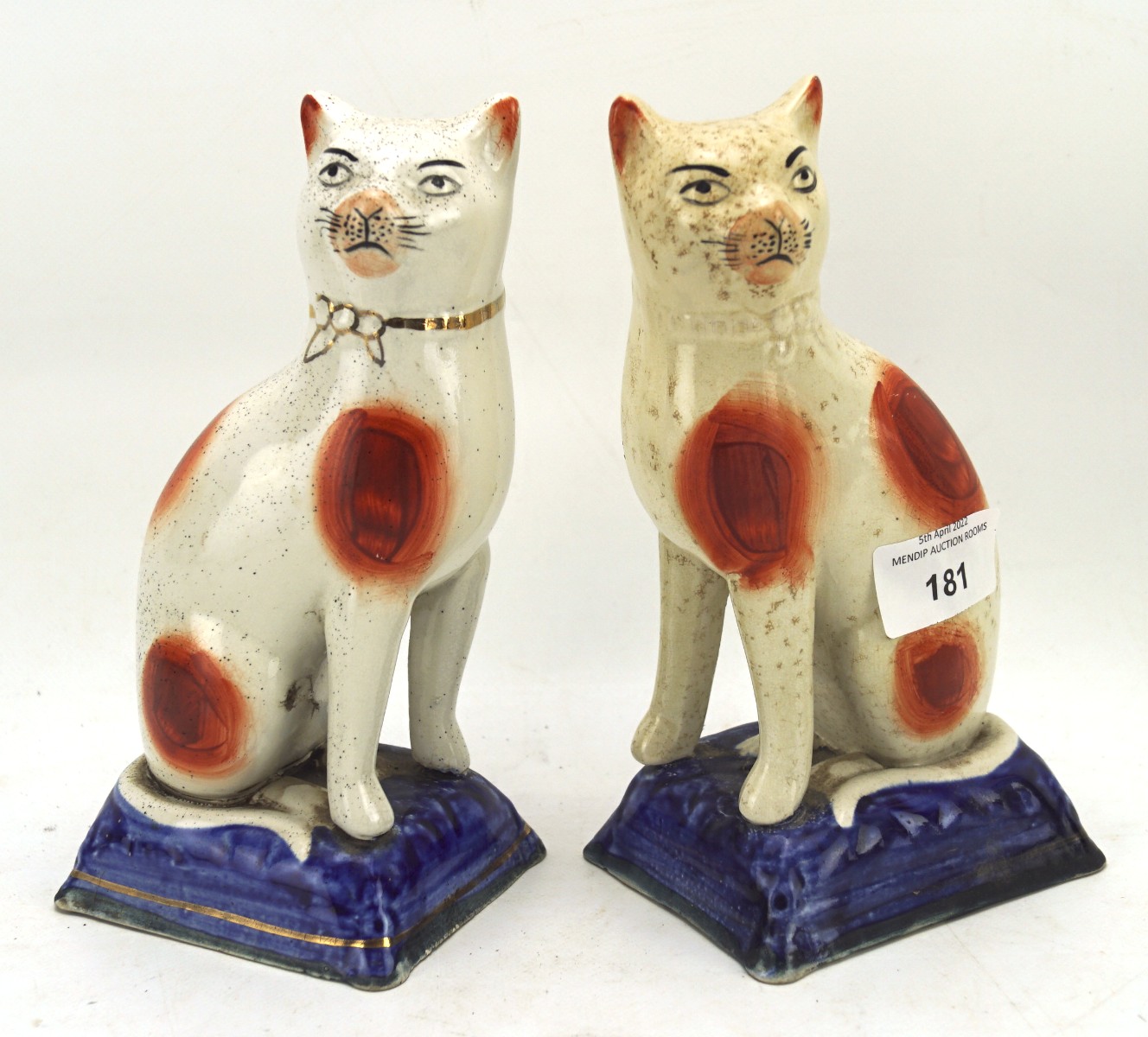 A pair of 19th century Staffordshire figures of cats, each seated upon a blue cushion,