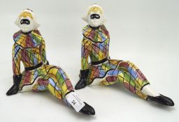 A pair of Italian ceramic figures of harlequins, in seated poses,