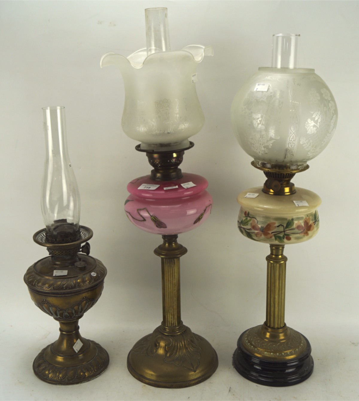 Three early 20th century brass oil lamps, two having painted coloured glass reservoirs,