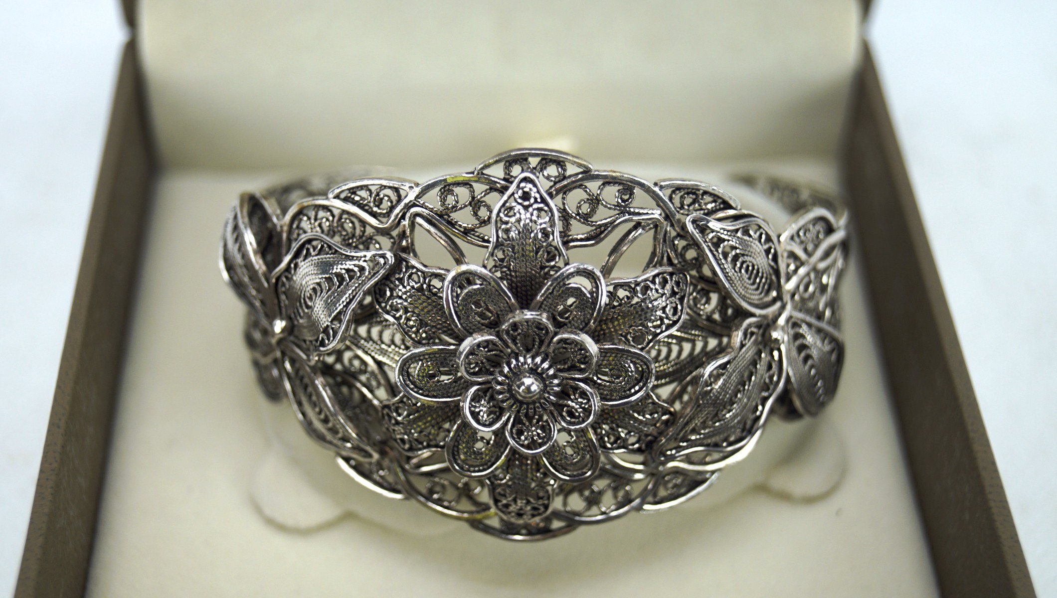 An ornate white metal filigree bangle, modelled as a flower,