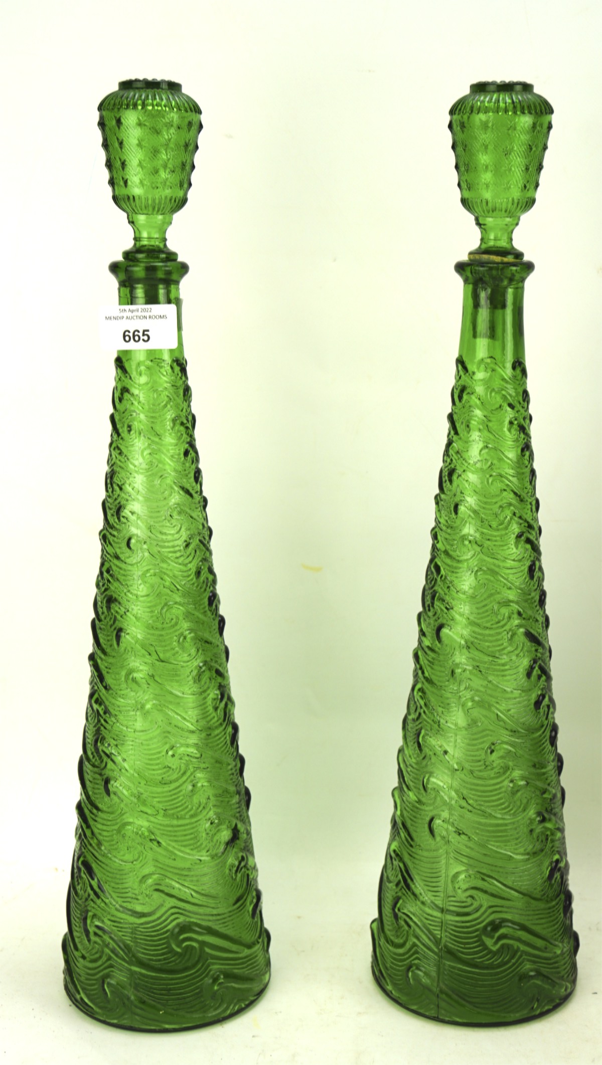 A pair of tall Italian green glass bottle and stoppers decorated in relief with a wave pattern,