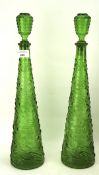 A pair of tall Italian green glass bottle and stoppers decorated in relief with a wave pattern,