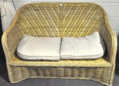 A contemporary wicker sofa, with a curved back and two cream cushions,