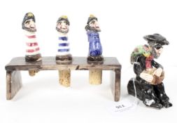 Three West Country Alan Young pottery wine stoppers and stand and a seated pirate