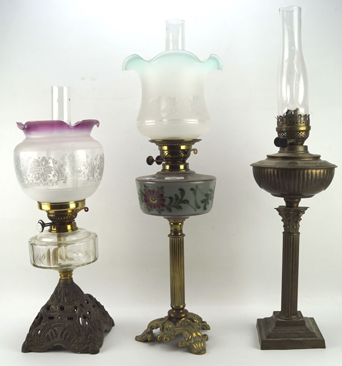 Three Edwardian oil lamps, two on gilt-metal fluted column bases, the third on pierced raised base,