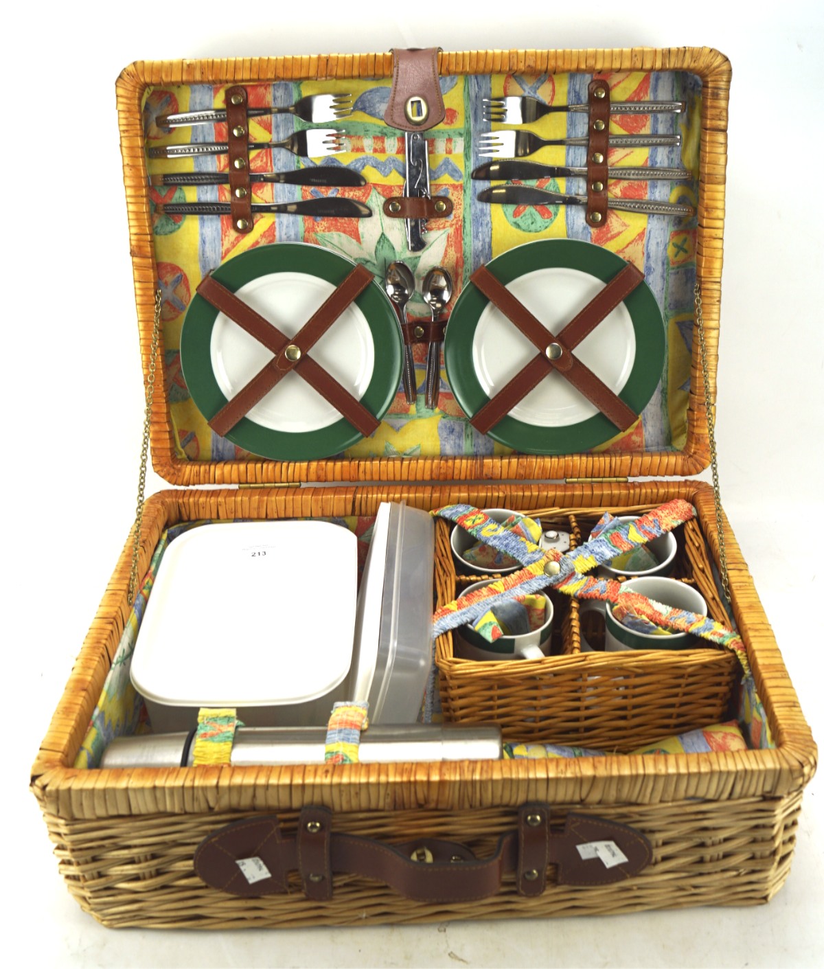 A wicker picnic basket with contents, including plates, thermos, mugs, cutlery and other items,