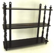 An early 20th Century ebonised three tier hanging wall shelf with turned supports and finials,