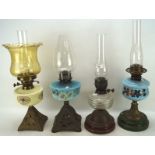 Four Edwardian oil lamps, two with blue glass bodies, one ivory and another clear,