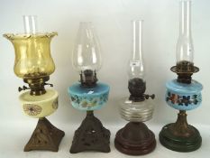 Four Edwardian oil lamps, two with blue glass bodies, one ivory and another clear,