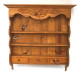 A rack of pine wall shelves with two shelves over three drawers, all beneath a carved, shaped panel,