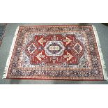 A red ground floor rug, with floral and geometric motifs and tassels to either end,