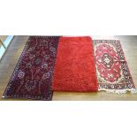 Three floor rugs, two being red, another purple, two with floral decoration,