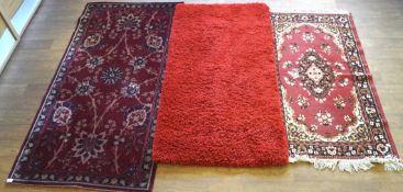 Three floor rugs, two being red, another purple, two with floral decoration,