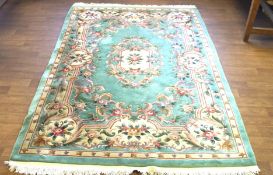 A large turquoise ground rug decorated with floral and foliate patterns, tassels at either end,