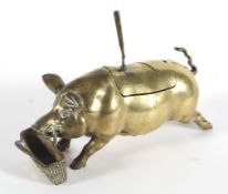 An inkwell or cruet stand cast as a brass pig before a basket spoon or pen-rest, with glass liner,