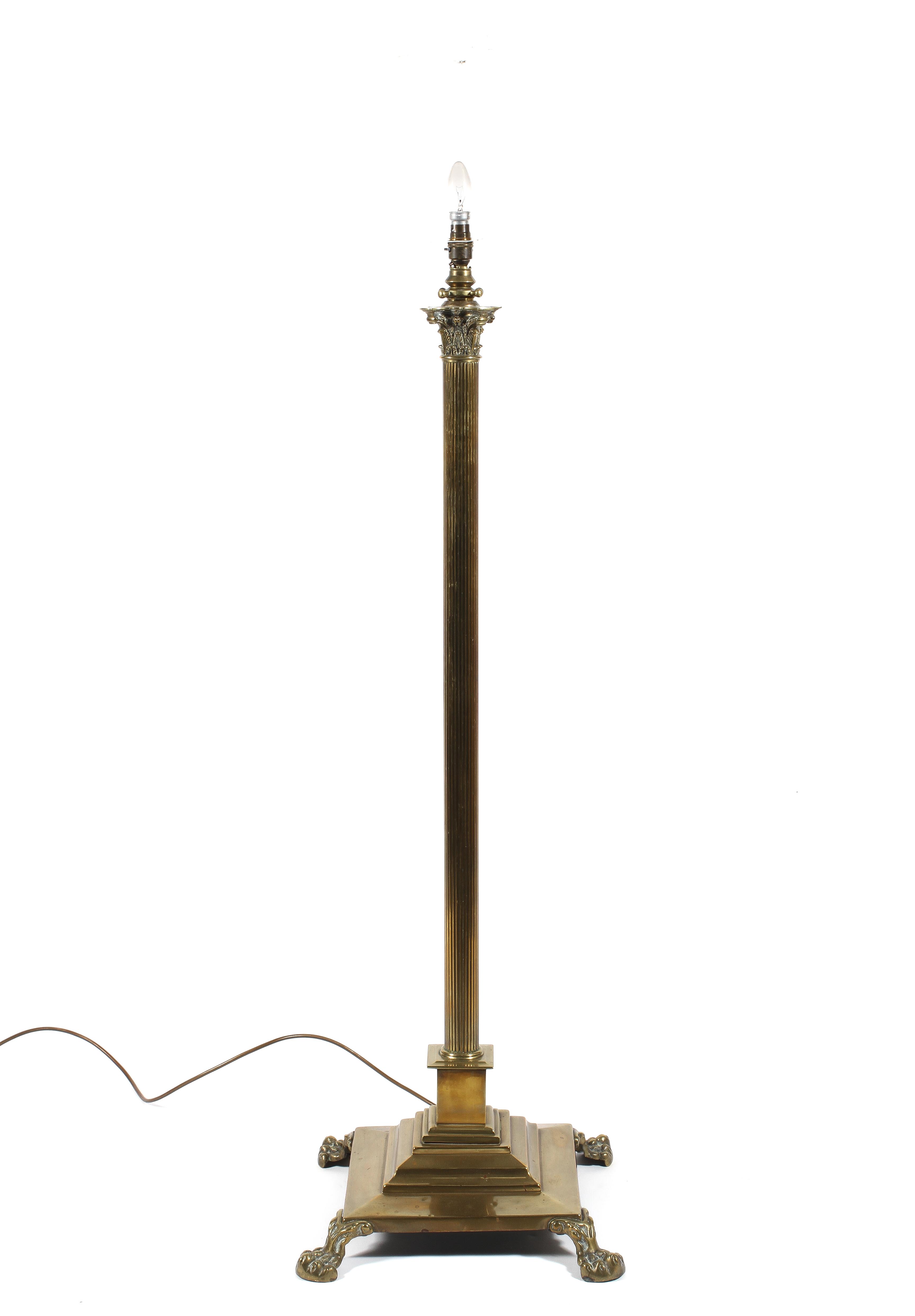 A brass corinthian column standard lamp, raised on lion paw feet,