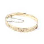 A 9ct gold bangle with engraved decoration and a safety chain,