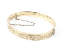 A 9ct gold bangle with engraved decoration and a safety chain,