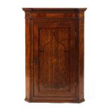 An 18th century inlaid oak wall corner cupboard the paneled door decorated with a central shell
