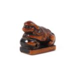 A small 19th century wood netsuke of a shishi resting its front paws on a bell,