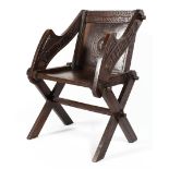 An oak Glastonbury elbow chair with carved inscription raised on X frame supports,