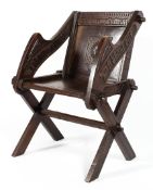 An oak Glastonbury elbow chair with carved inscription raised on X frame supports,