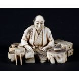 A late 19th century Japanese carved ivory okimono, depiciting a cross-legged cobbler and his wares,