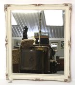 A contemporary mirror with white painted carved wood frame.